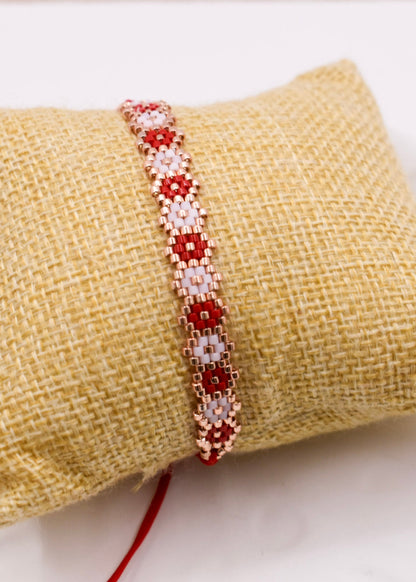 Beaded bracelet with red and white pattern on a textured beige surface