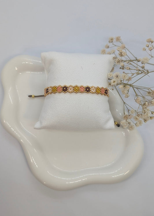Bracelet on a white pillow with a decorative dish and flowers on a light gray background