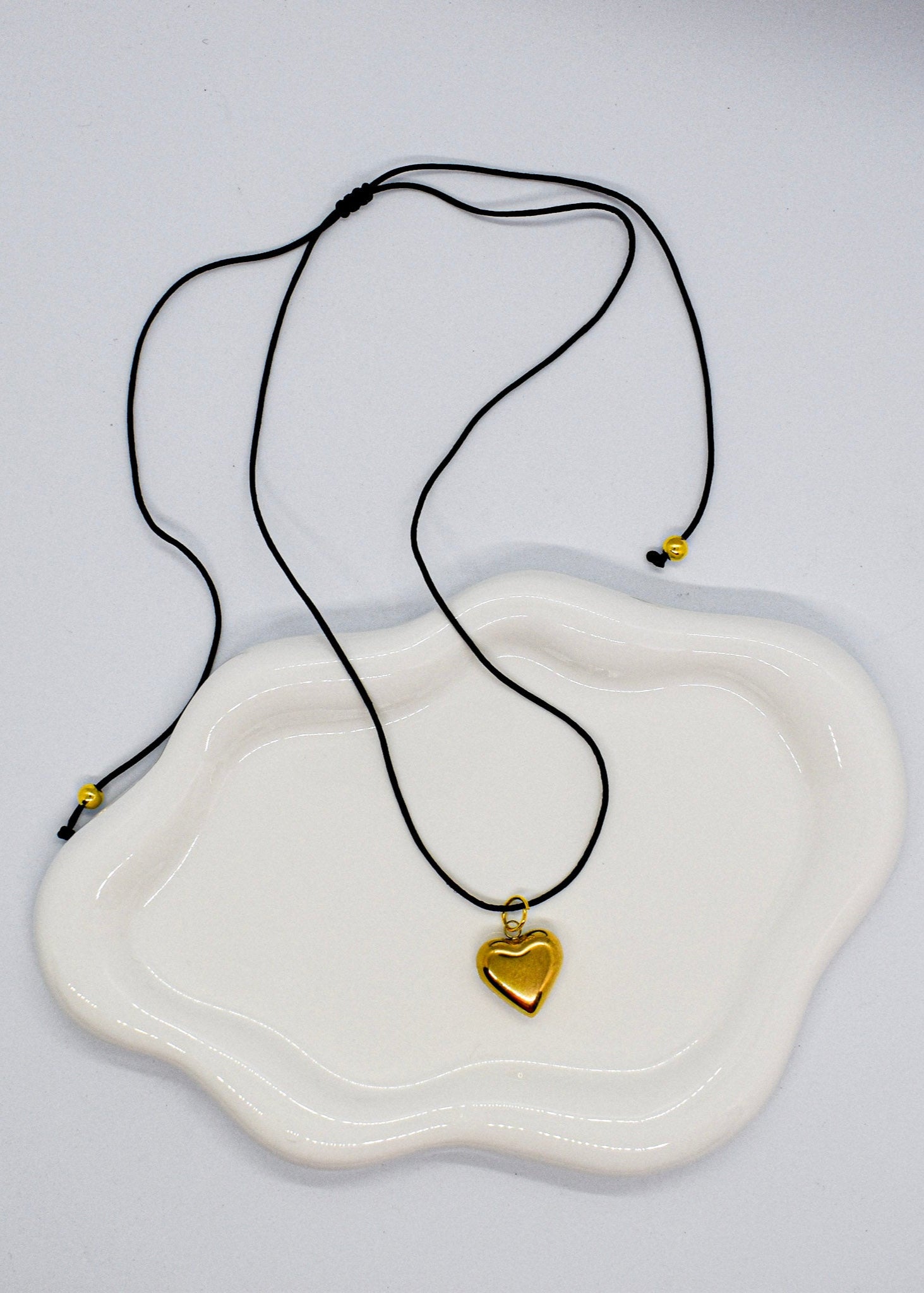 Necklace with a gold heart pendant on a white dish against a light gray background