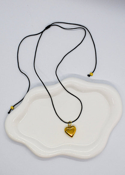 Necklace with a gold heart pendant on a white dish against a light gray background