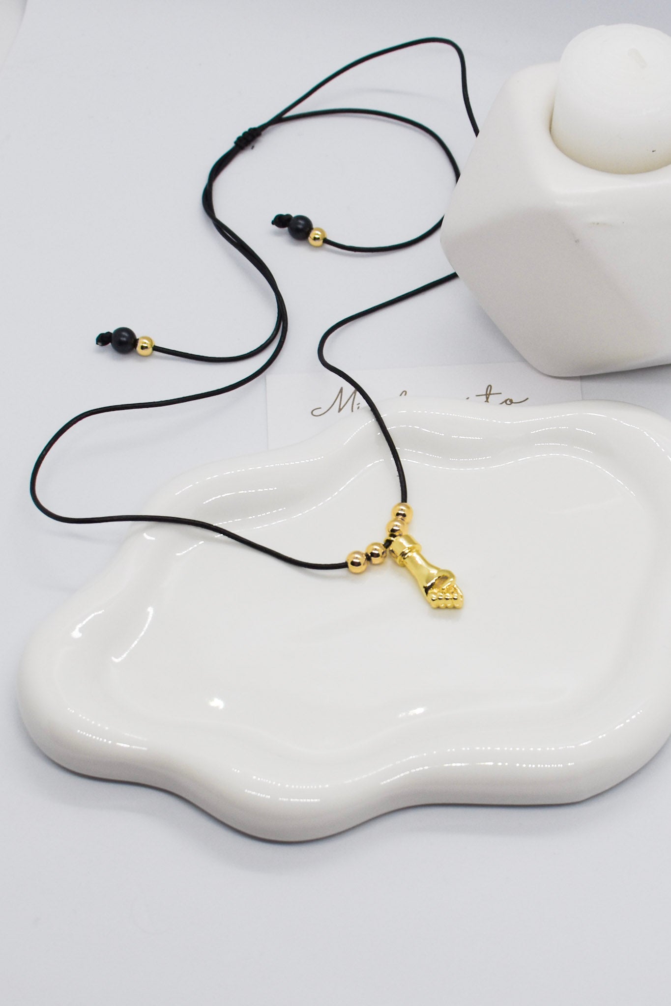 Necklace with a gold pendant on a white ceramic dish, with 'Minta' branding.