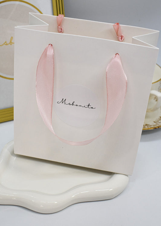 White gift bag with pink handles on a white surface