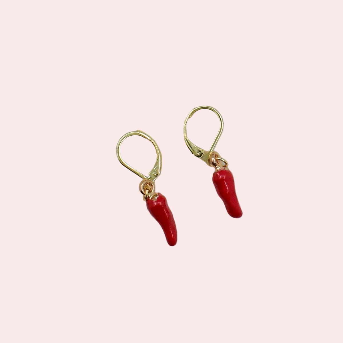 A pair of gold leverback earrings with dangling red chili pepper charms, shown on a solid pale pink background.