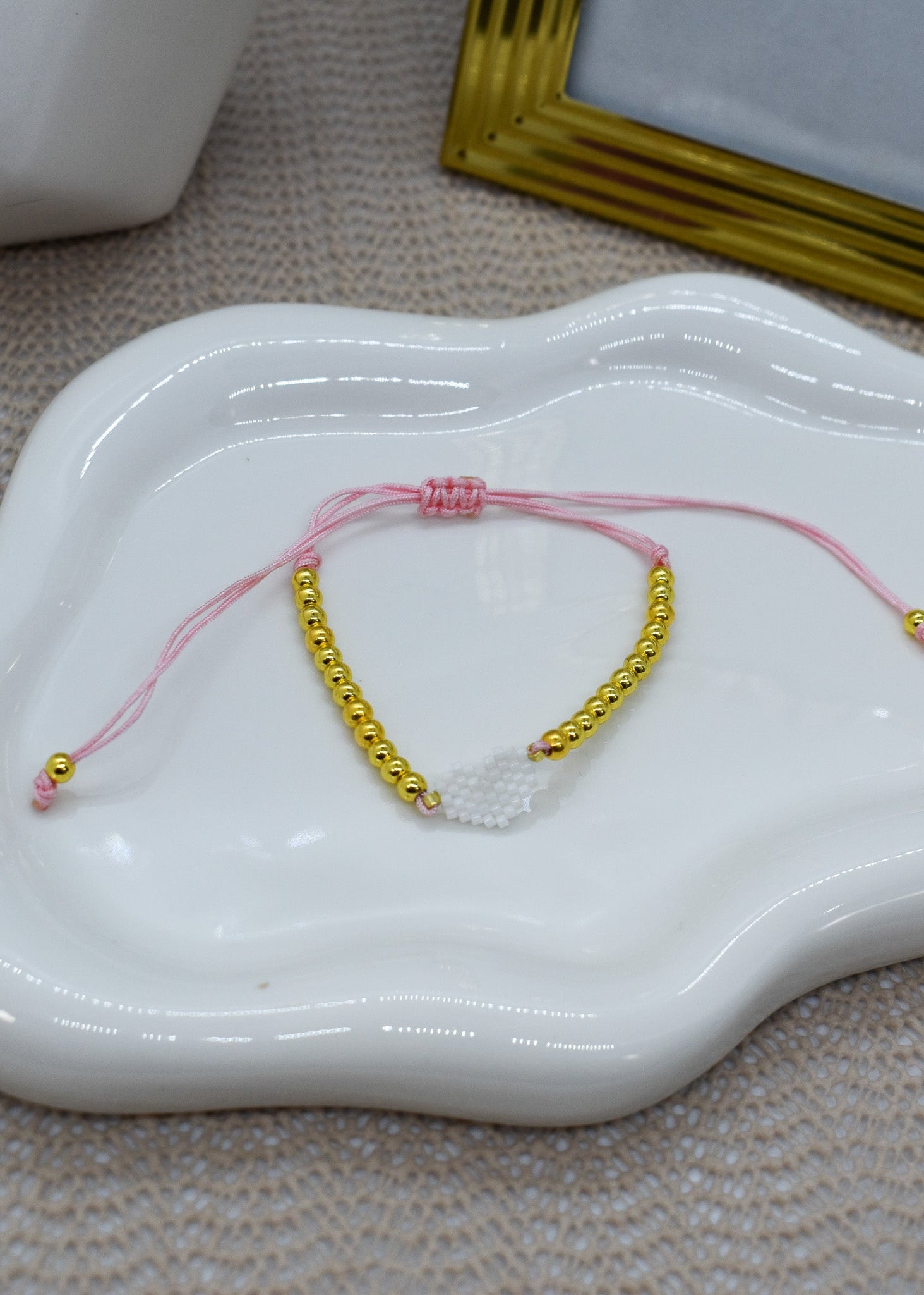 pink bracelet wit with gold beads, on a white ceramic dish.