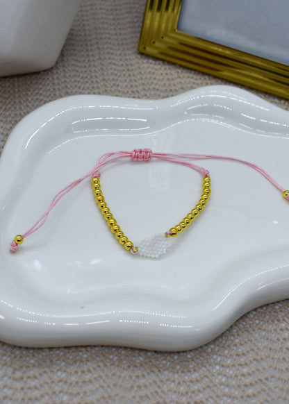 pink bracelet wit with gold beads, on a white ceramic dish.