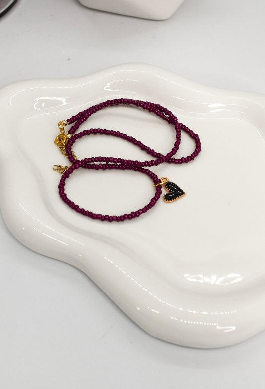 Purple beaded bracelet with heart charm on a white dish