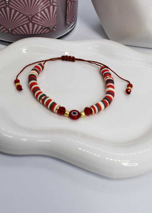 red beads bracelet with evil eye bead on a white tray and aa candle 