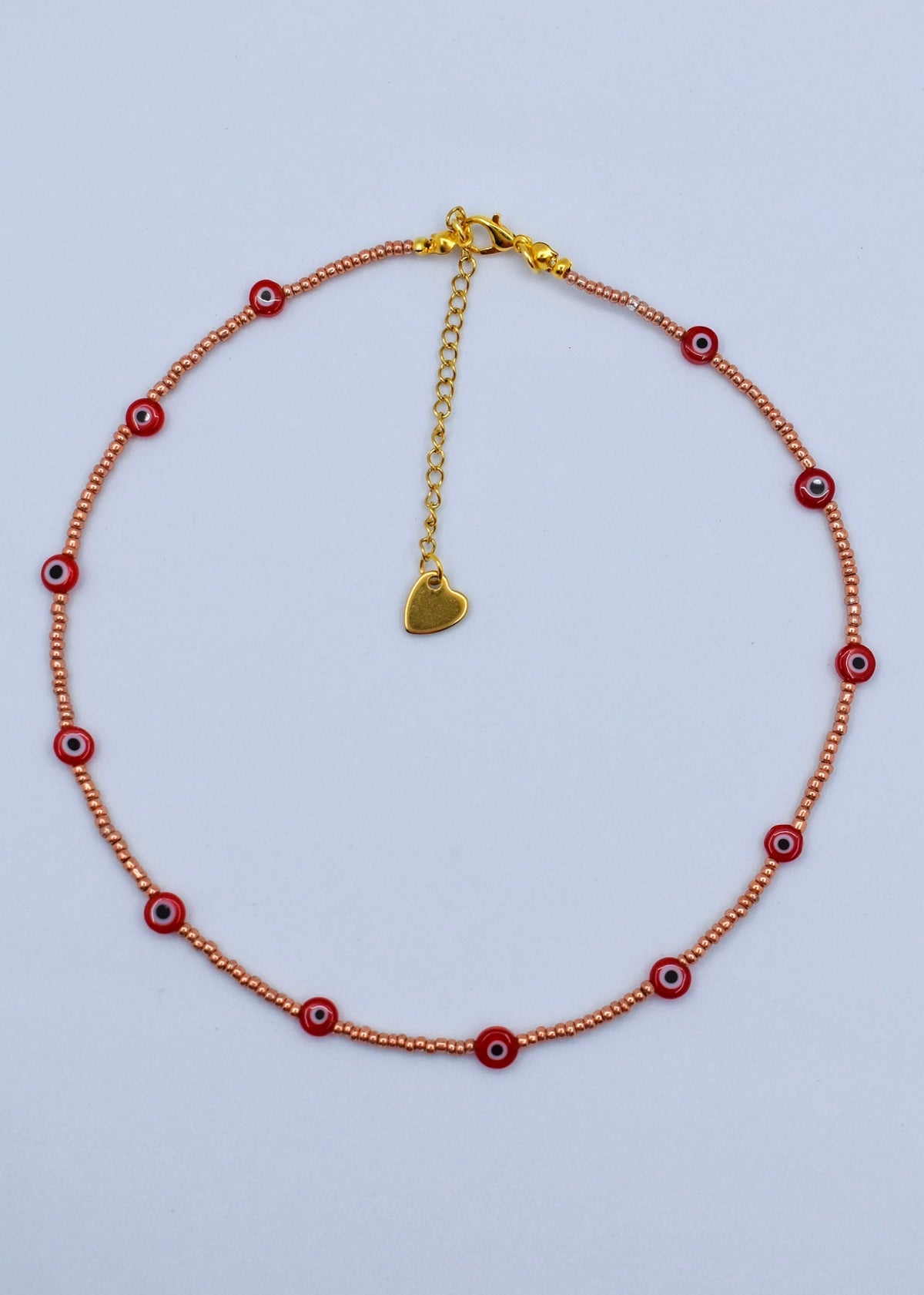 red evil eye necklace with golden beads on a white surface