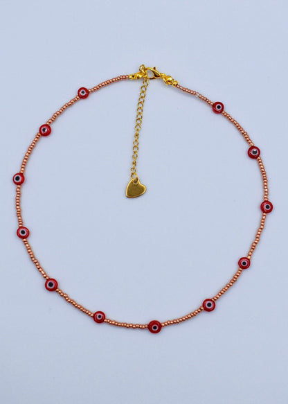 red evil eye necklace with golden beads on a white surface
