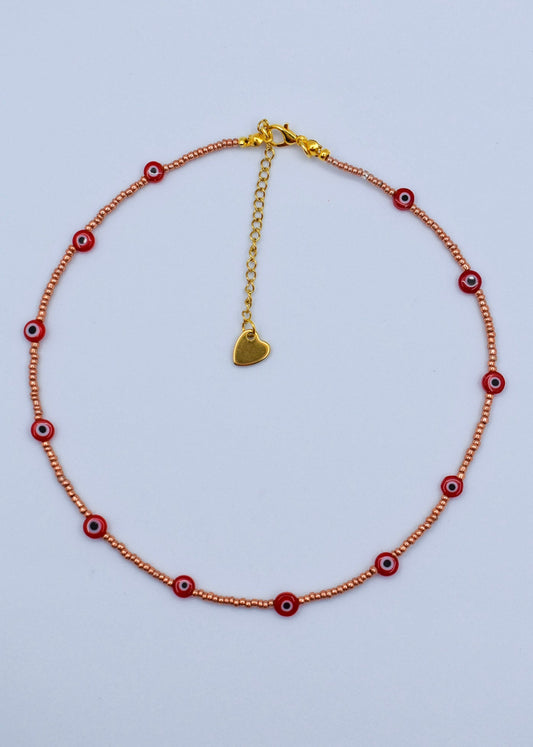 red evil eye necklace with golden beads on a white surface