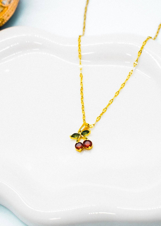 Gold necklace withred cherry pendant on a white dish