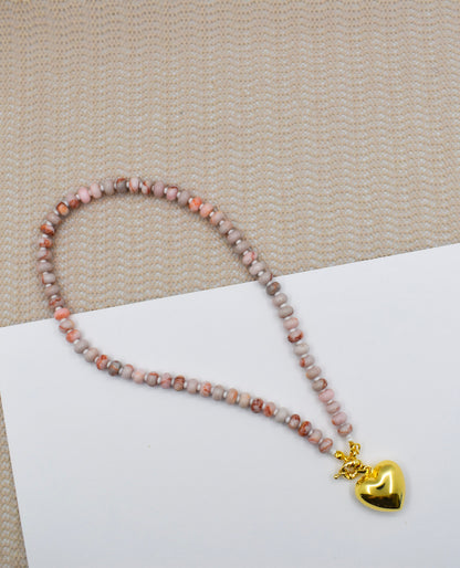 Necklace with heart-shaped gold charm on a beige surface