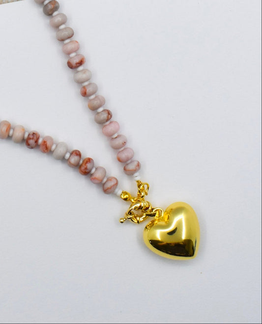 Necklace with heart-shaped gold charm on a beige surface