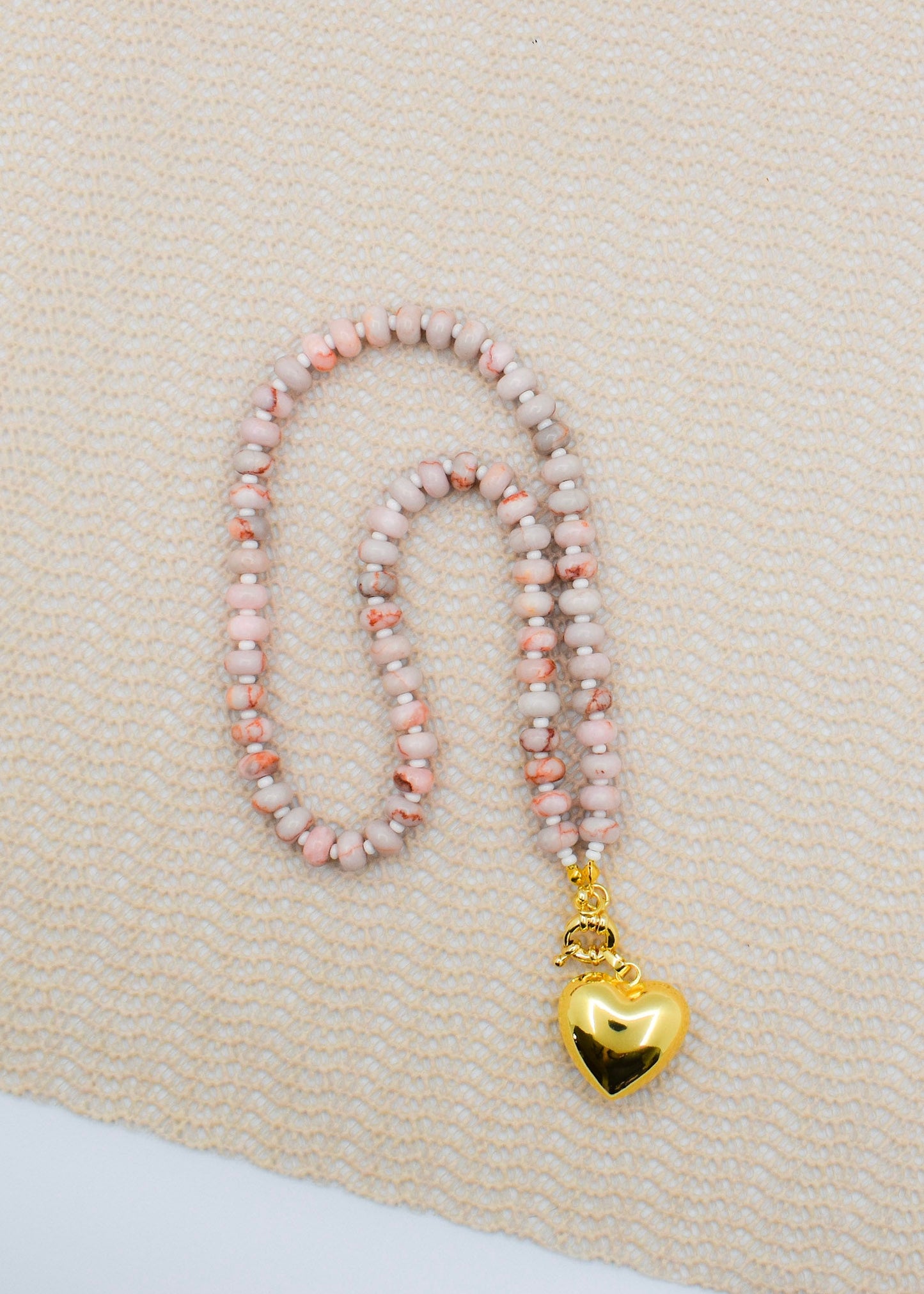 Necklace with pink beads and a gold heart pendant on a beige fabric background