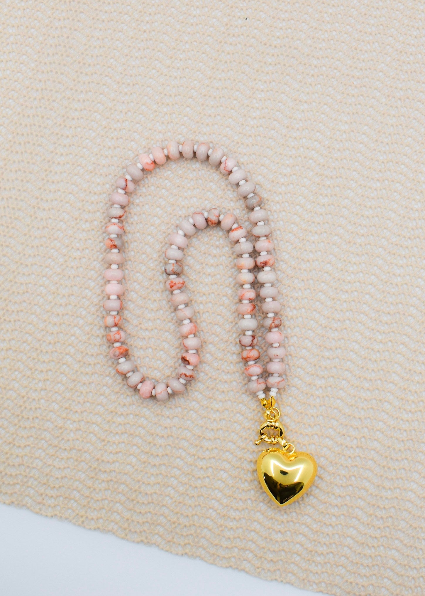Necklace with pink beads and a gold heart pendant on a beige fabric background