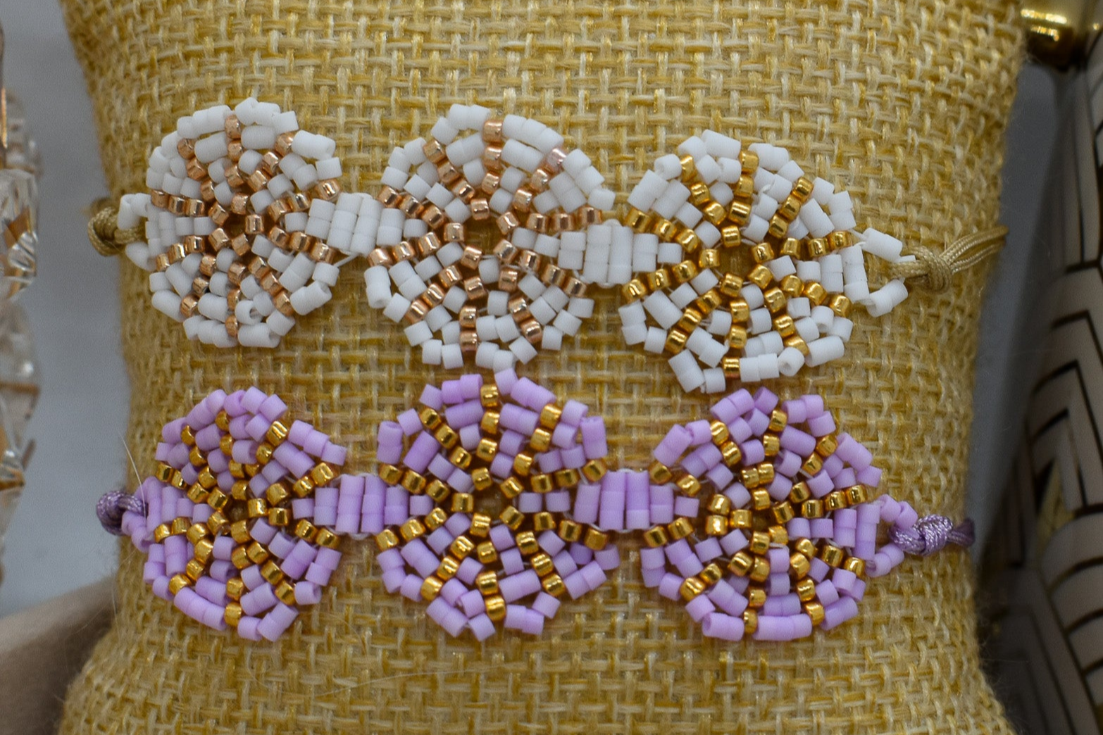 Beaded bracelet with white, gold, and purple flowers on a textured yellow background