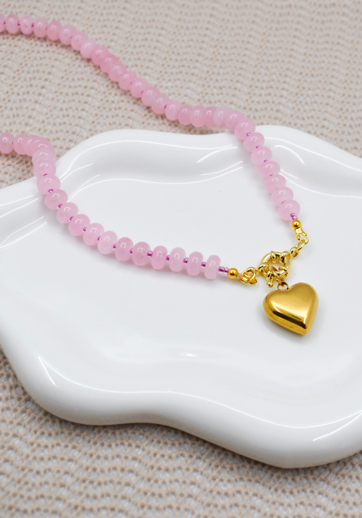 rose quartz necklace with a gold heart charm on a white dish.