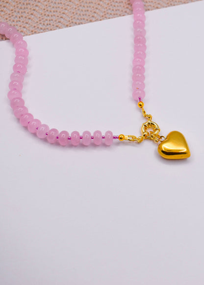 Rose quartz necklace with a gold heart charm on a white surface