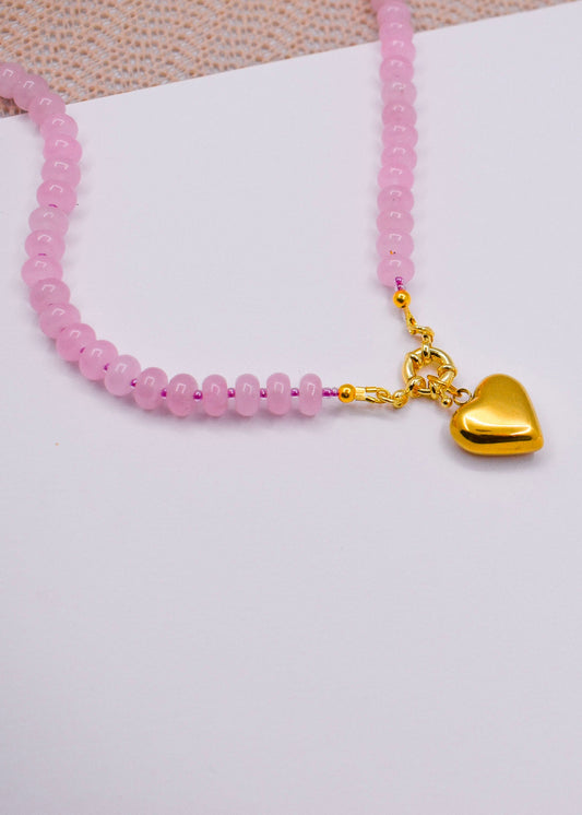 Rose quartz necklace with a gold heart charm on a white surface