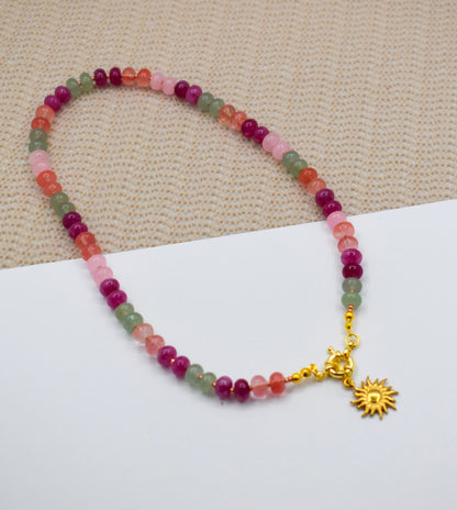 Multicolored beaded bracelet with a gold sun charm on a beige fabric background