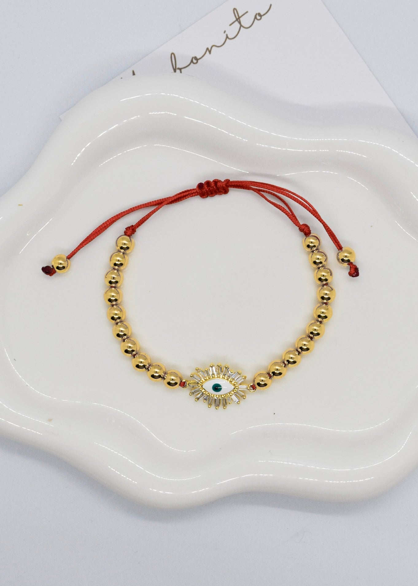 Gold beaded bracelet with a central stone on a white dish, branded 'hanita'.