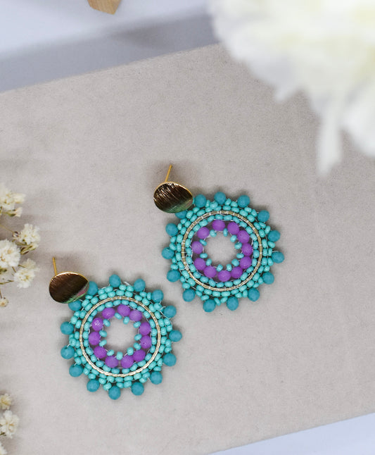 Turquoise and purple beaded earrings on a light gray surface with white flowers.