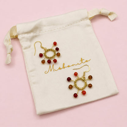 Gold and red beaded earrings on a white drawstring bag with 'Mehendi' branding.