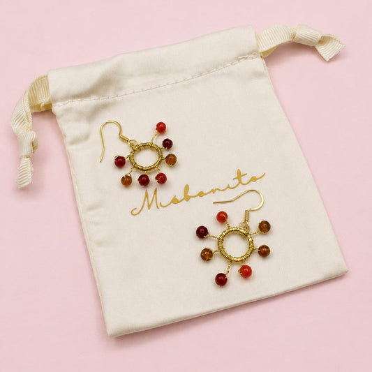 Gold and red beaded earrings on a white drawstring bag with 'Mehendi' branding.