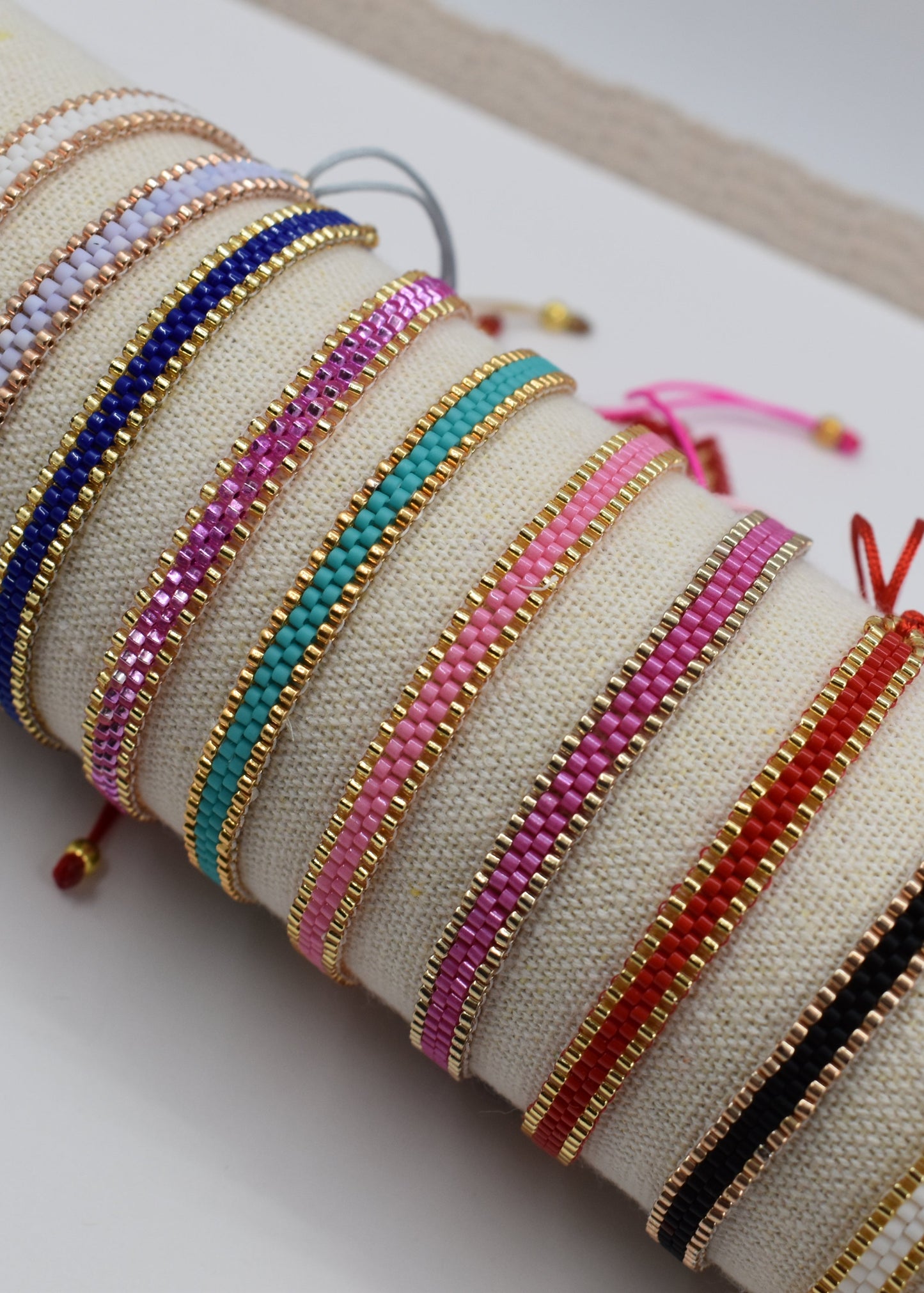 A collection of colorful beaded bracelets displayed on a beige fabric roll-up stand against a clean white background.