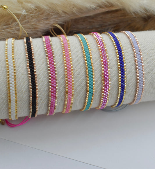 A set of beaded bracelets displayed on a cream fabric roll-up stand. The bracelets feature gold-plated metal links with seed beads in various colors including black, pink, mint green, purple, and light blue.
