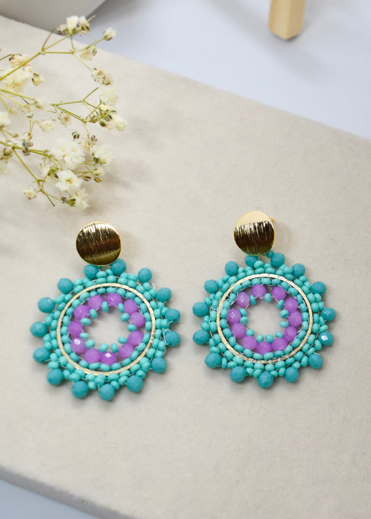Turquoise and purple beaded earrings on a light surface with white flowers.