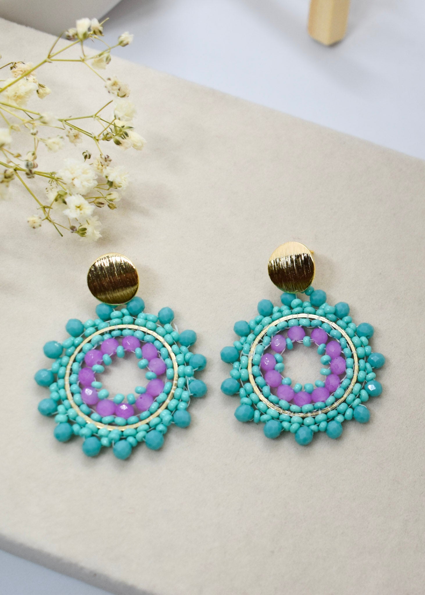 Turquoise and purple beaded earrings on a light surface with white flowers.